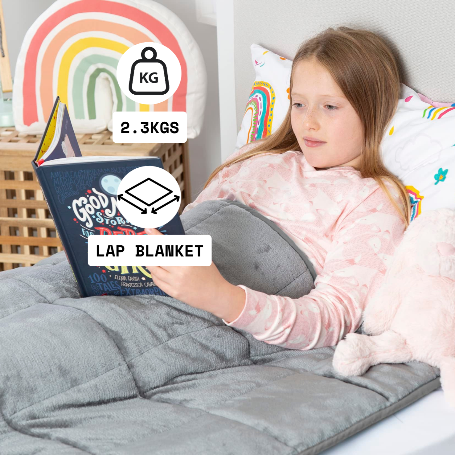 Child reading a book on a gray weighted lap blanket with rainbow elements in the background