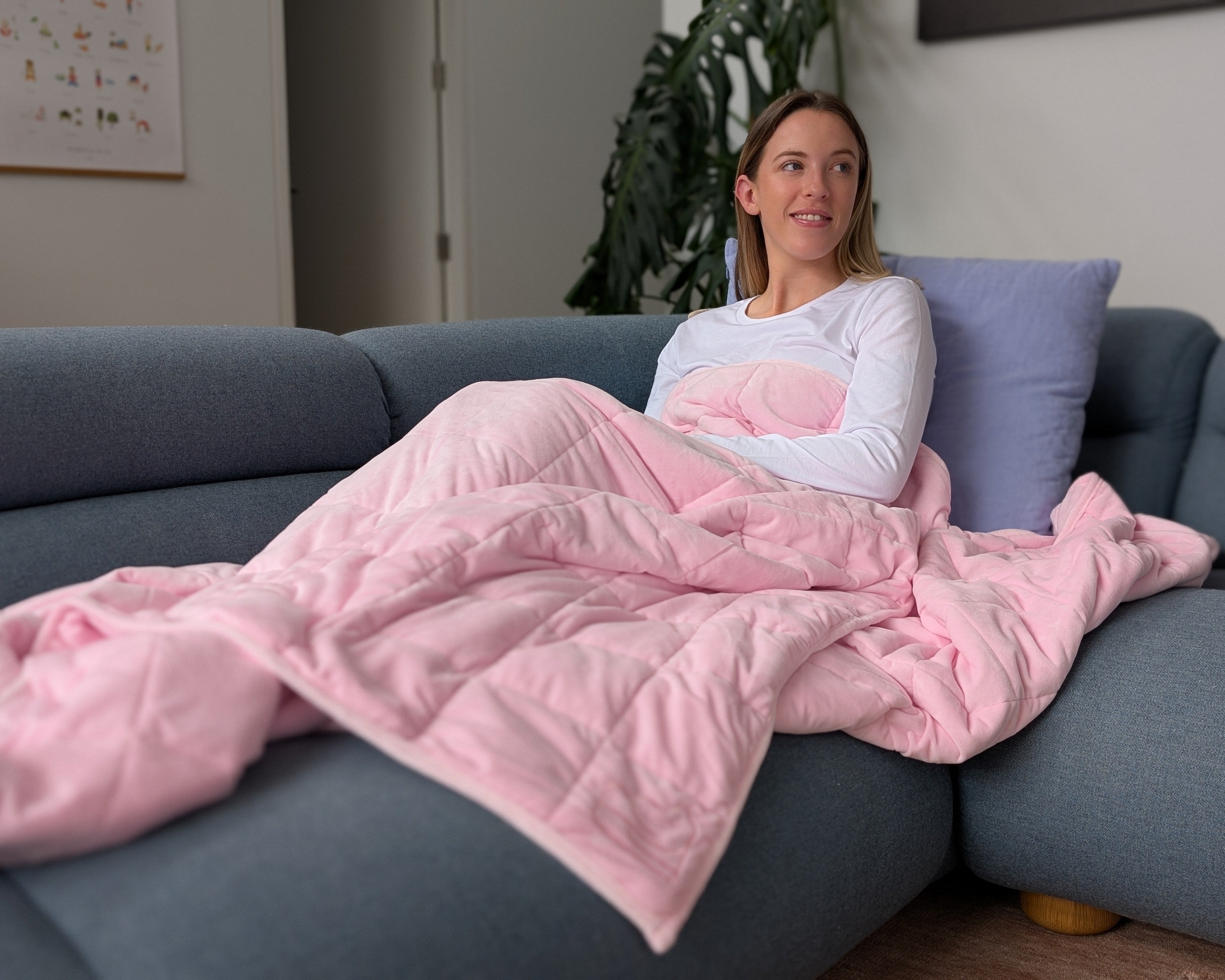 Woman sitting on a couch under a pink weighted blanket in a cozy living room.